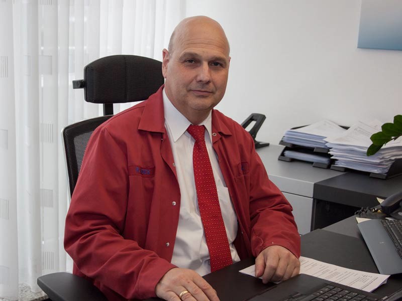 Mann in roter Jacke und mit roter Krawatte sitzt am Schreibtisch 